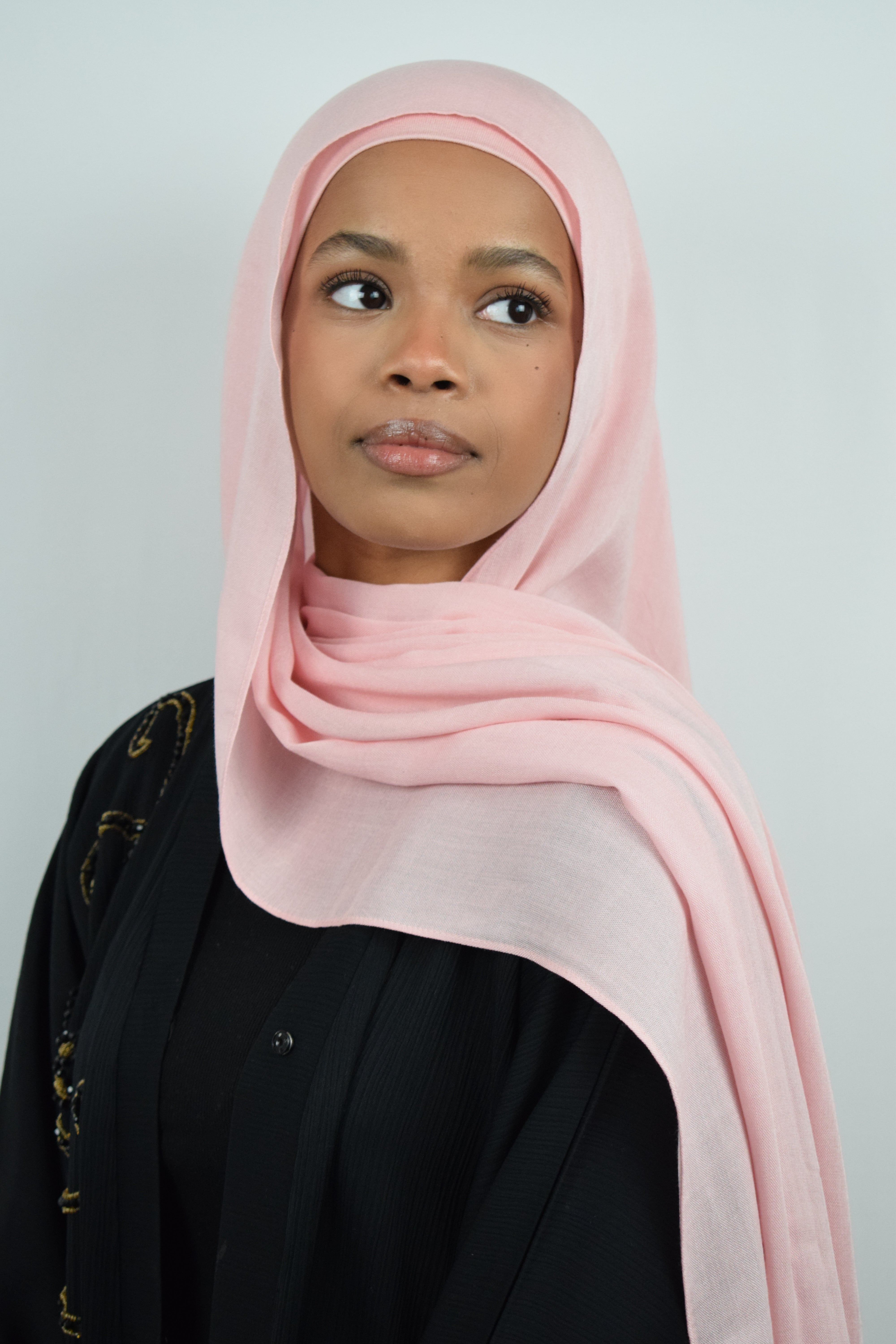 Woman wearing a pink hijab on a plain background