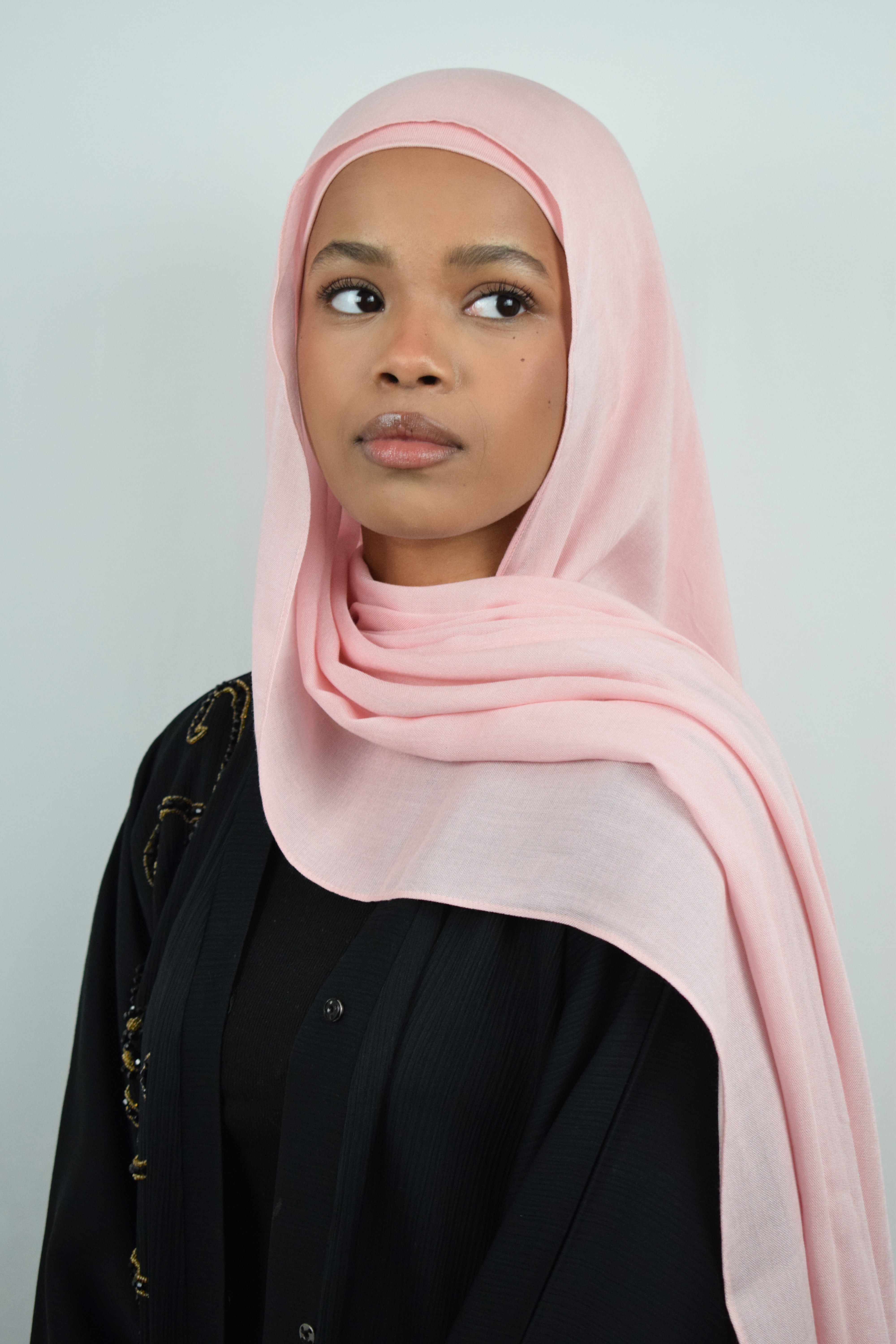 Woman wearing a pink hijab and black outfit against a light gray background