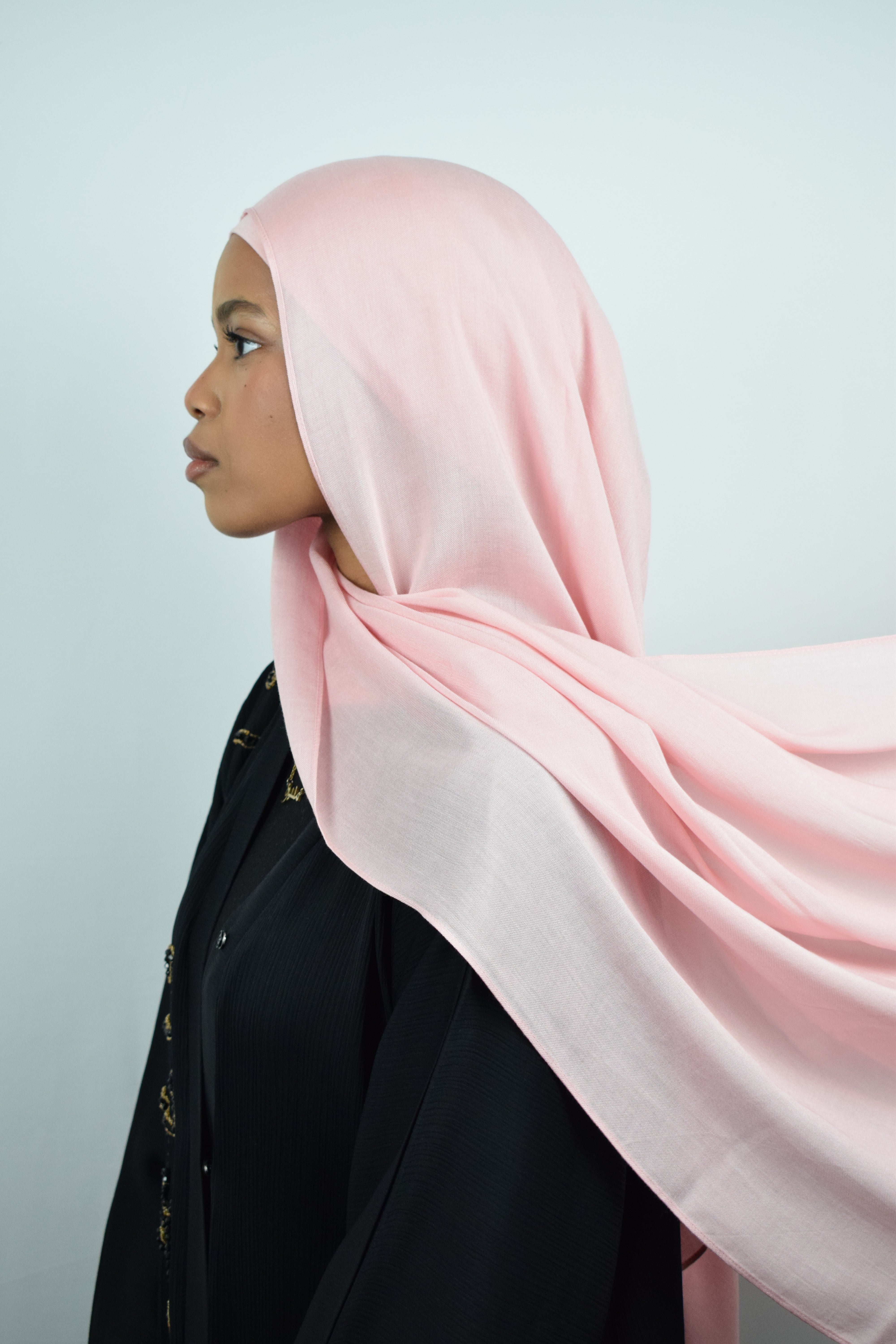 Woman wearing a pink hijab and black outfit against a light gray background