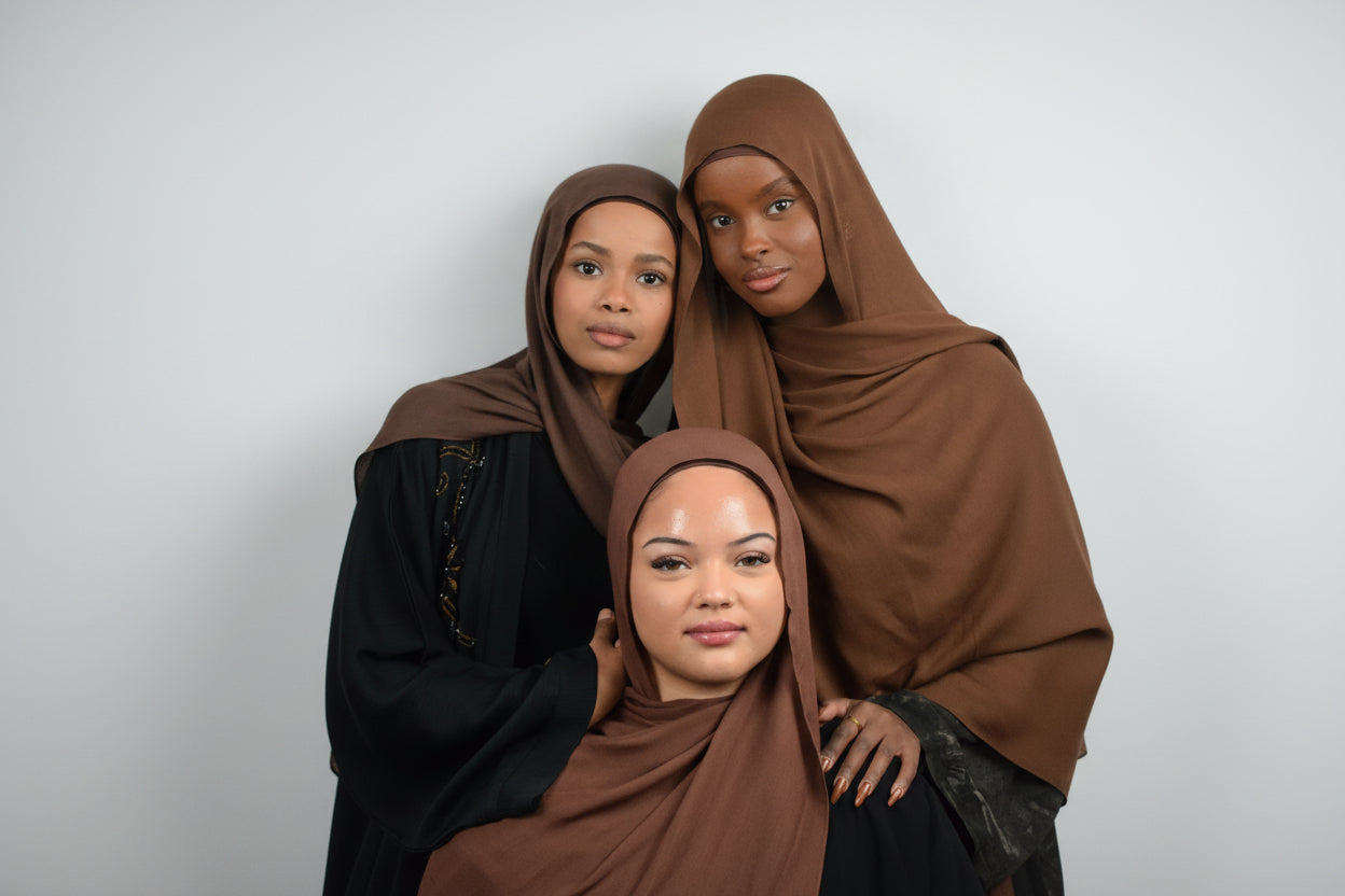 Three women wearing brown hijabs posing together against a white background